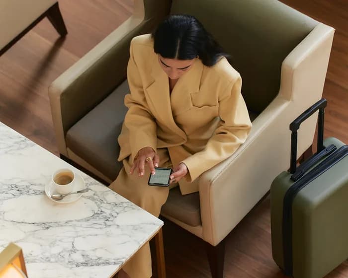 Viajera sentada en un sillón consultando el móvil junto a su maleta